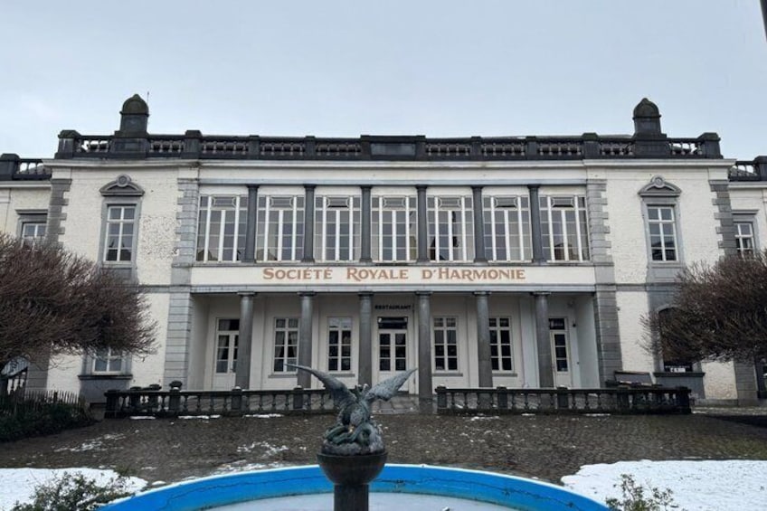 A large building with the sign 'SOCIETE ROYALE D'HARMONIE' and a fountain in the foreground. 4