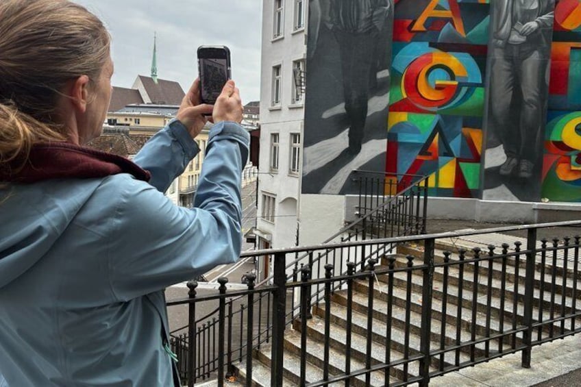 A person taking a photo of a colorful mural on a building. 1