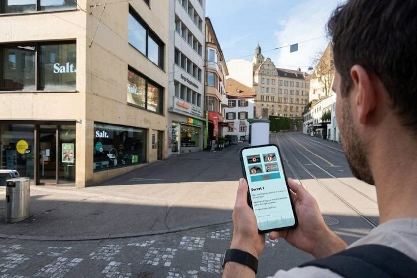 A person holding a smartphone with a map application, standing on a street with buildings and a tram track. 3