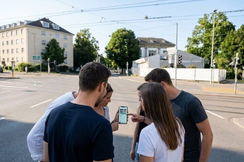 A group of people standing on a street corner, looking at a smartphone. 4