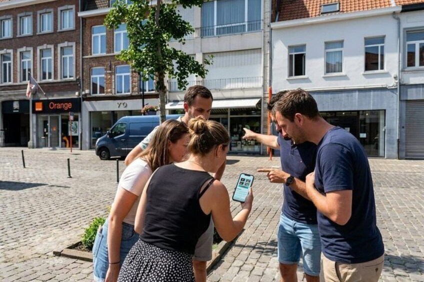A group of people standing on a cobblestone street, looking at a smartphone. 5