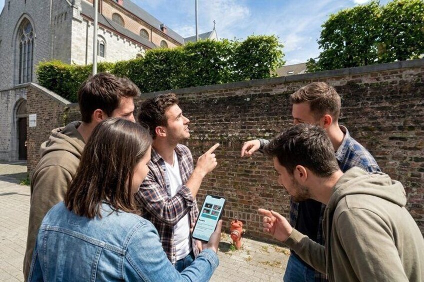 A group of people taking a photo with a smartphone in front of a brick wall and a church. 2