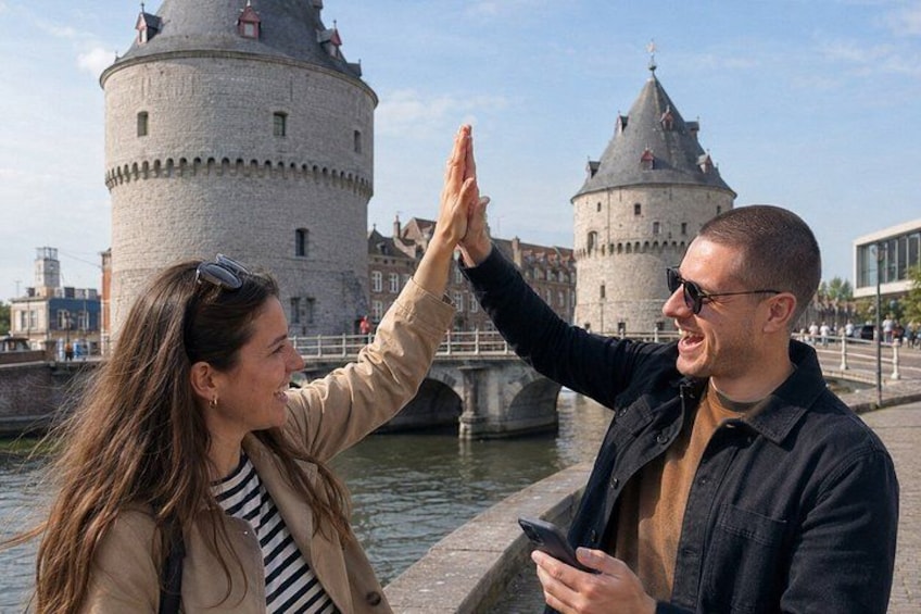 A couple taking a high-five near a historic tower by a body of water. 1