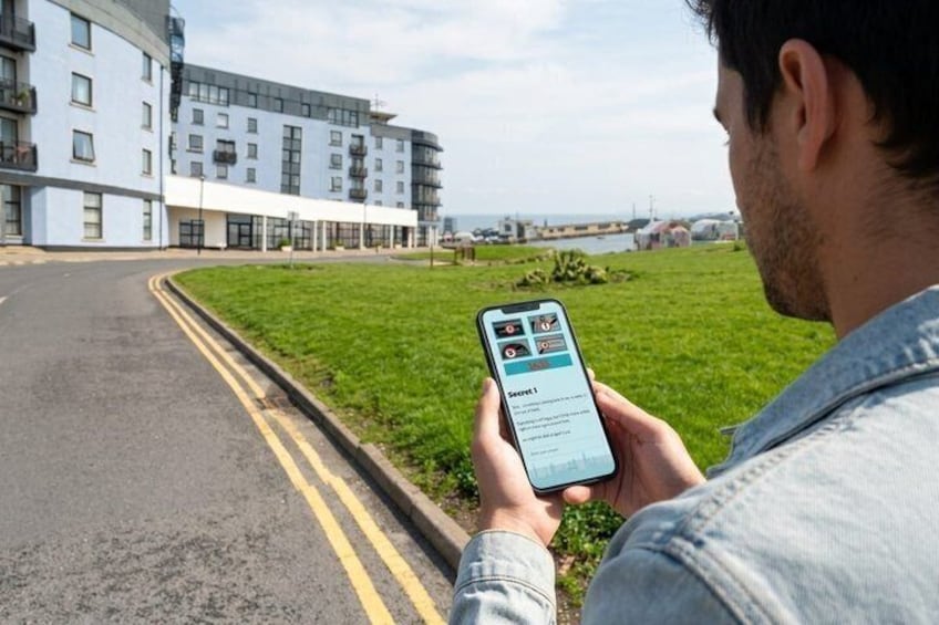 A person holding a smartphone with a map application, a road, a grassy area, and a building in the background. 3