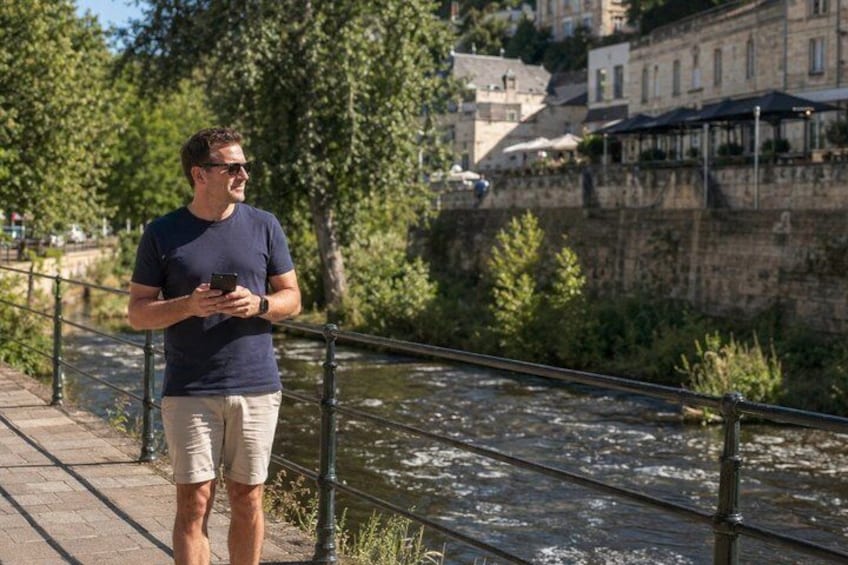 A man standing by a river with a railing, holding a smartphone. 1