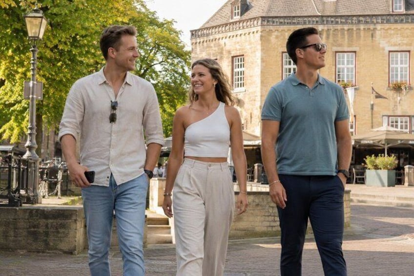 Three people walking on a paved path in a public square with buildings and trees in the background. 4