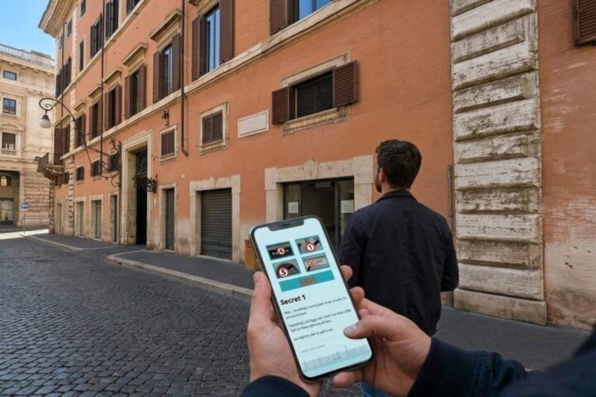 Eine Person hält ein Smartphone mit einer Karten-App in der Hand und steht auf einer Kopfsteinpflasterstraße vor einem Gebäude mit einer Steinaußenfassade. 3