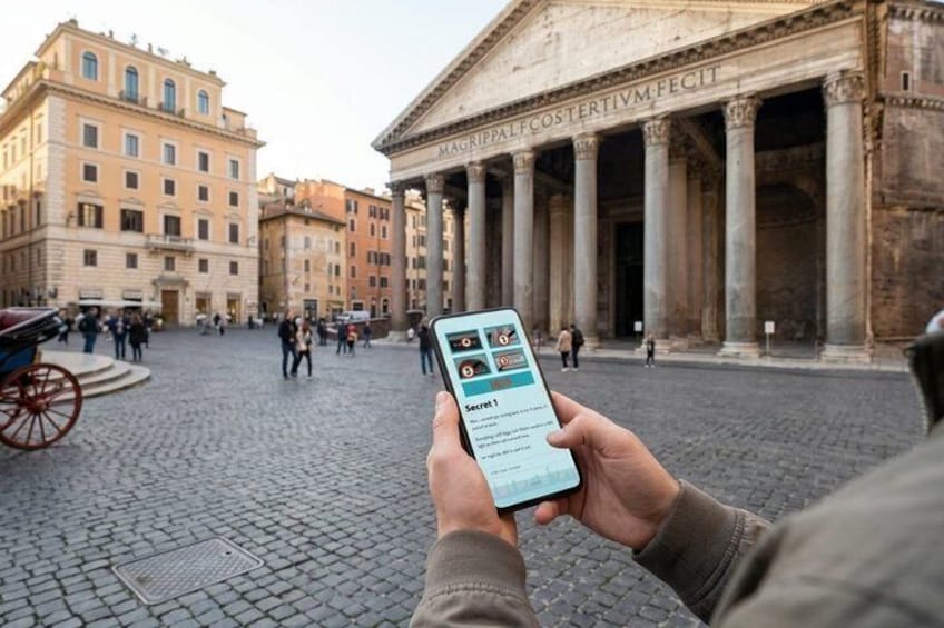 Eine Person hält ein Smartphone mit einer Karten-App in der Hand, steht auf einem Kopfsteinpflasterplatz mit historischen Gebäuden und Säulen im Hintergrund. 4