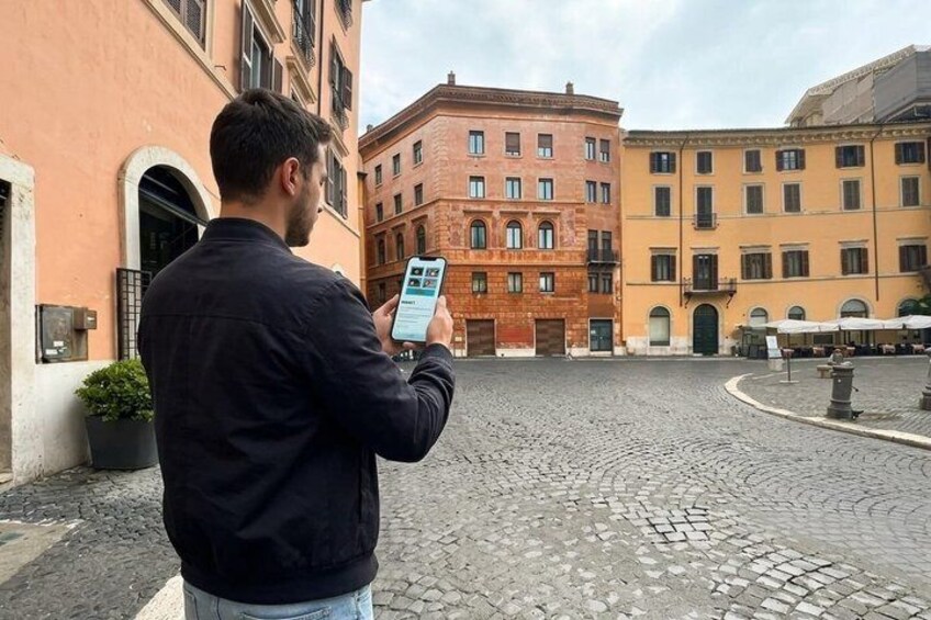Ein Mann benutzt ein Smartphone auf einem Kopfsteinpflasterplatz, umgeben von historischen Gebäuden. 5