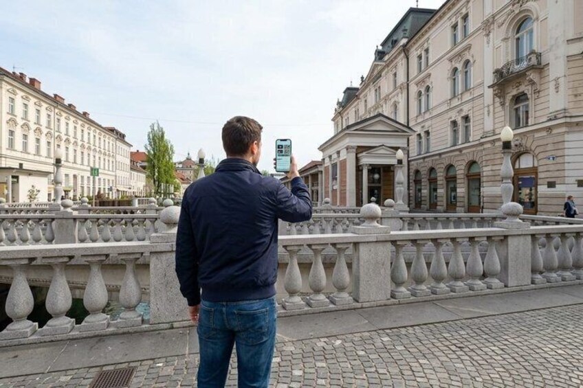 Een man maakt een foto met een smartphone op een brug met versierde balustrades en historische gebouwen op de achtergrond. 5