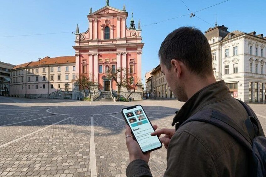 Iemand gebruikt een smartphone op een geplaveid straatje, met een roze historisch gebouw op de achtergrond. 2