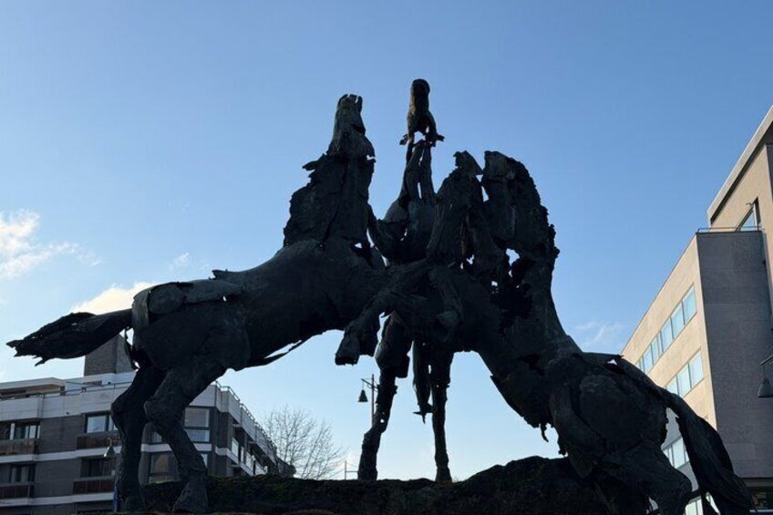 A sculpture of a horse and rider, with a building in the background. 1