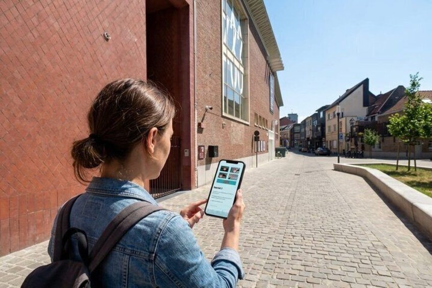 A person using a smartphone on a brick-paved street with buildings in the background. 2