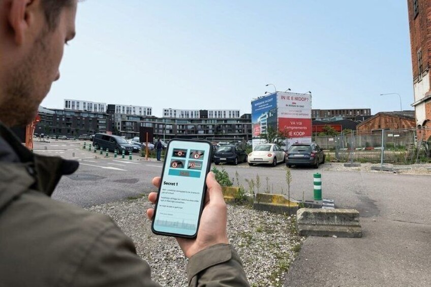 A person holding a smartphone with a map application, a parking lot with cars, and a building with a sign in the background. 3