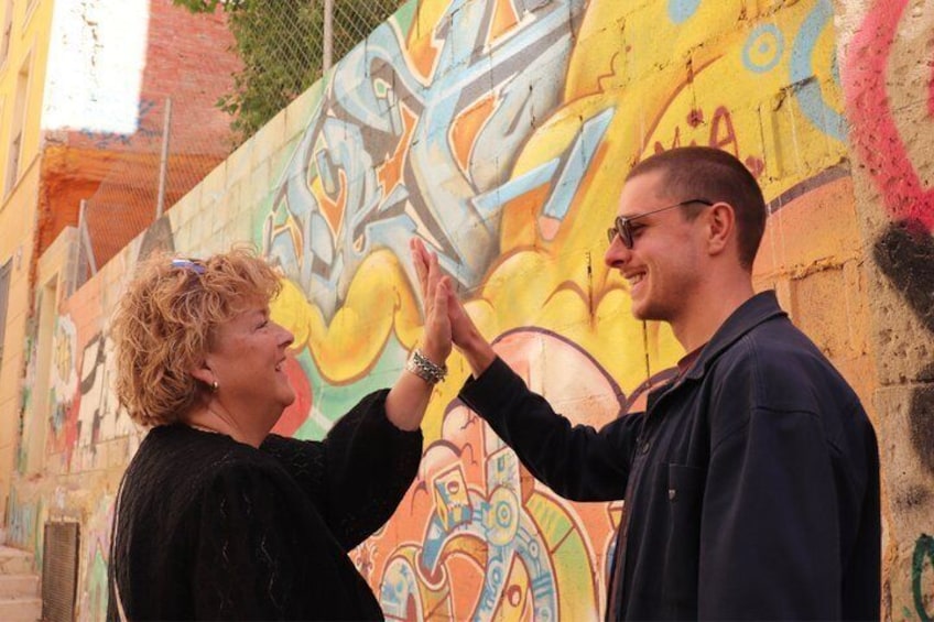 Twee personen geven elkaar een high-five voor een kleurrijke muurschildering. 1