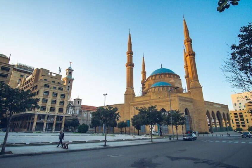 A mosque with a blue dome and four minarets, surrounded by urban buildings. 1