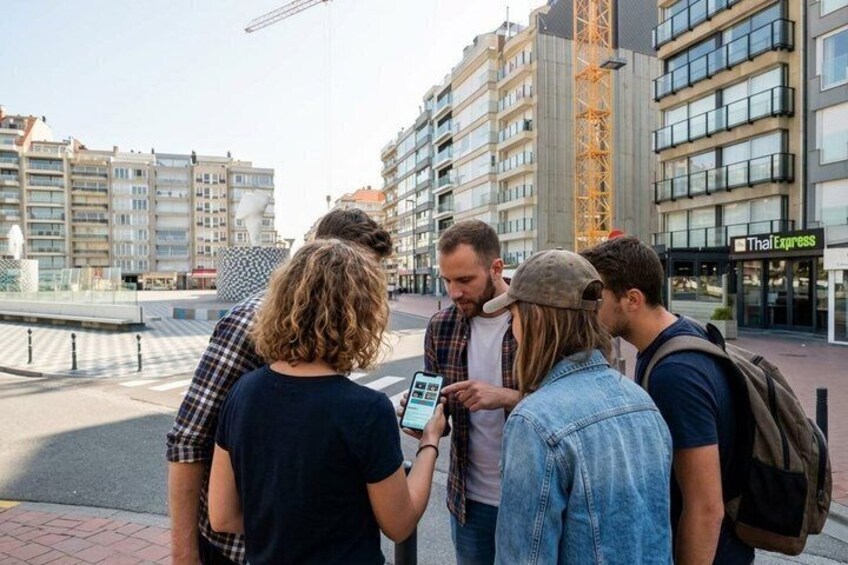 A group of people standing on a city sidewalk, looking at a smartphone. 2
