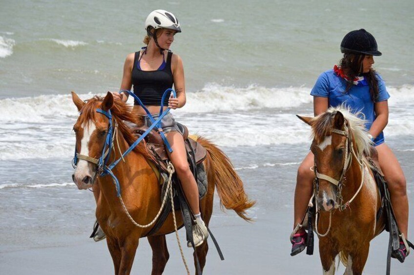 Deux personnes à cheval sur une plage, avec des vagues en arrière-plan. 3