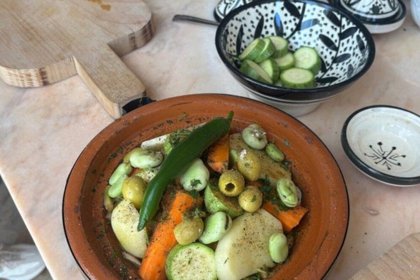 A terracotta dish with vegetables, a green chili, and olives. 5