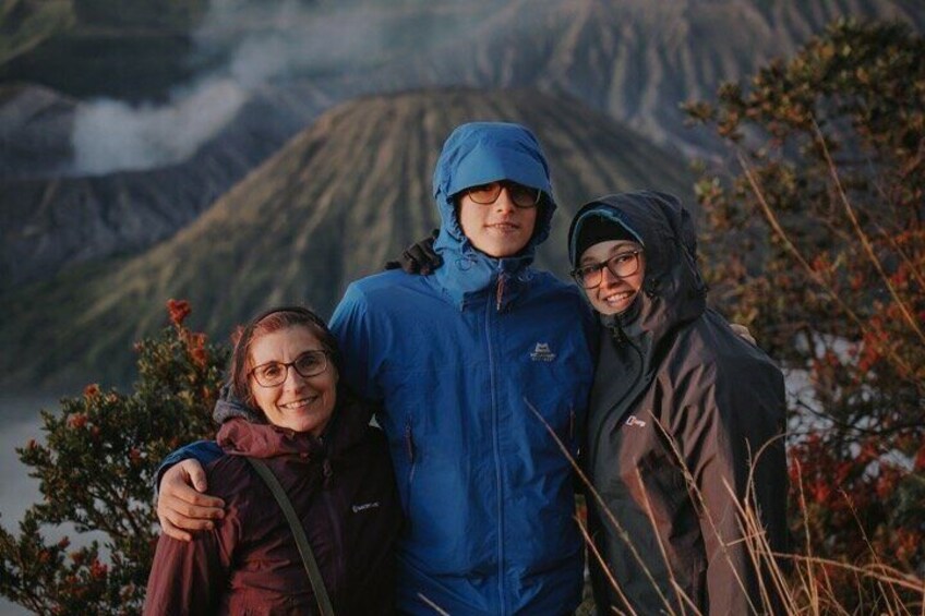 Three people standing on a mountain with a volcano in the background. 1