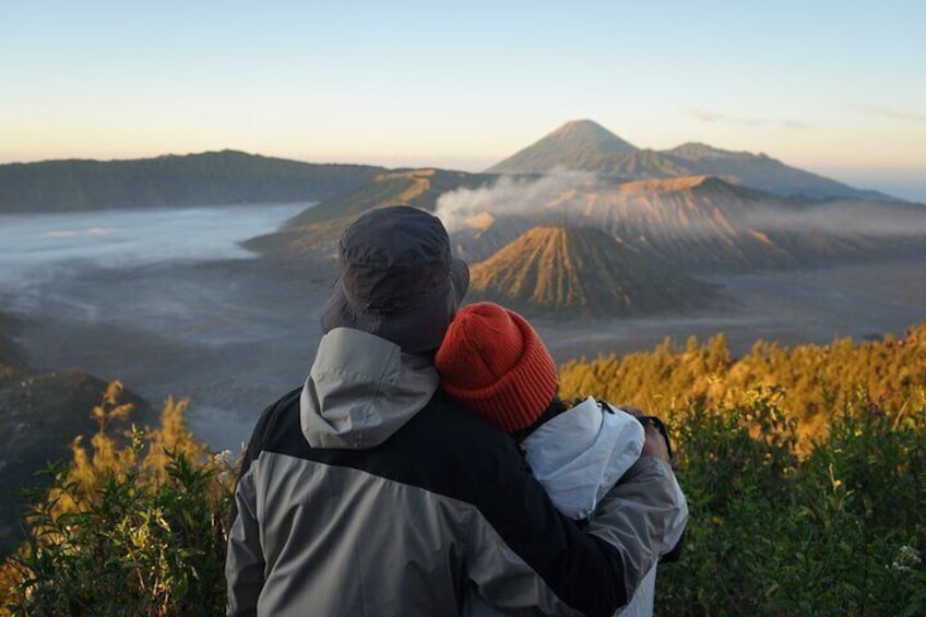 Two people embracing, overlooking a volcanic landscape with a mountain in the background. 1
