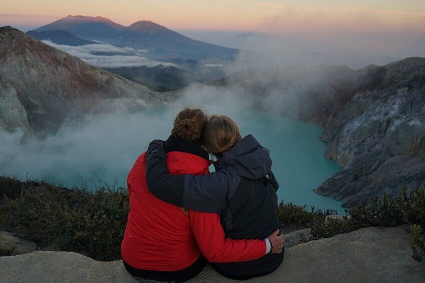Two people embracing on a mountain ledge overlooking a turquoise lake with mist. 4
