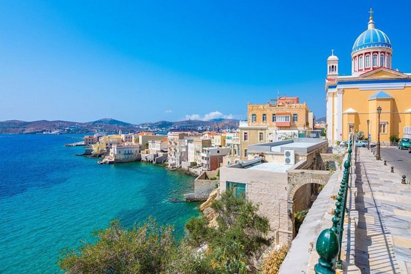 A coastal town with buildings, a clear blue sea, and a prominent church with a blue dome. 4