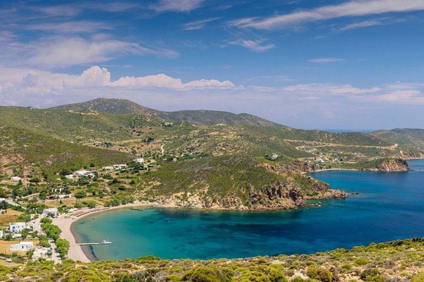 A coastal landscape with a beach, clear blue waters, and green hills. 3