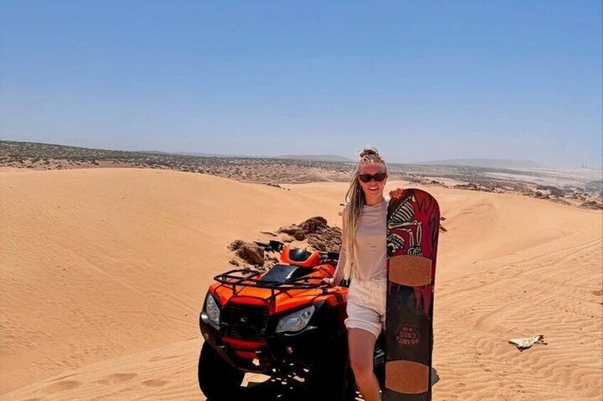 A person standing next to an ATV in a desert with sand dunes in the background. 3