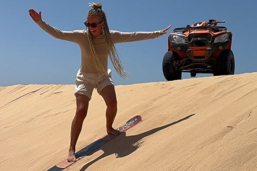 A person snowboarding on a sand dune with an ATV in the background. 4