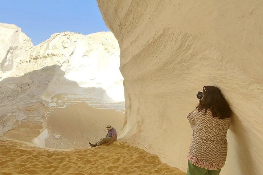 A person taking a photo inside a narrow canyon with a person sitting on the sand. 5