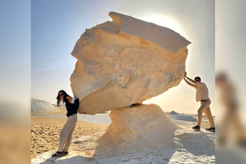 Two people balancing a large rock in a snowy landscape. 1