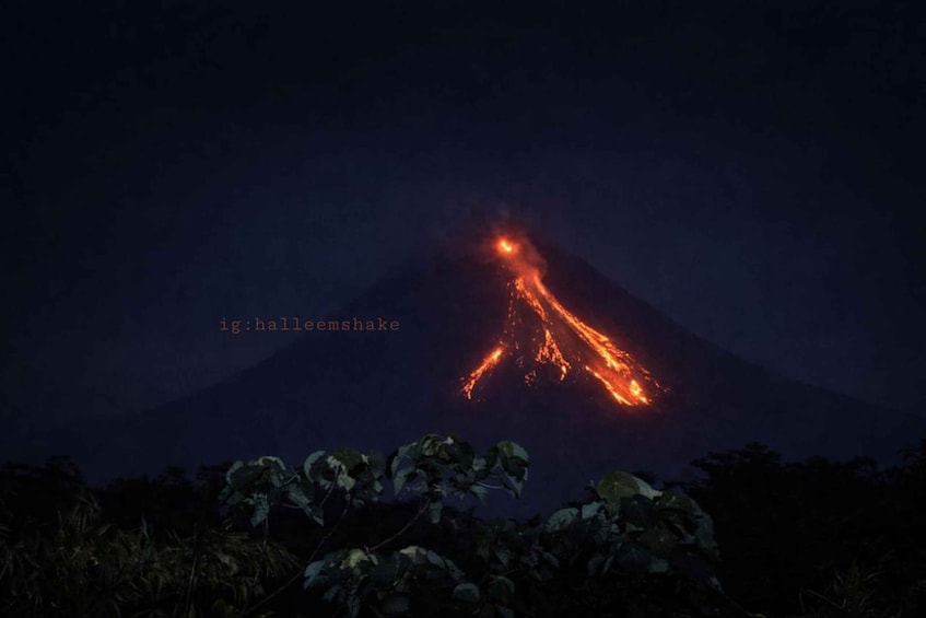 A volcano with lava flowing down its side at night. 4