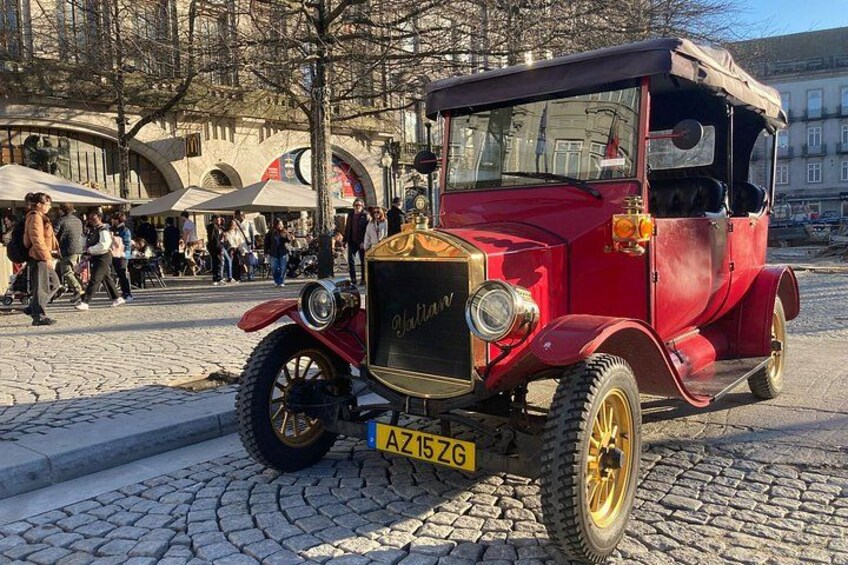 Un coche rojo antiguo estacionado en una calle adoquinada, con gente caminando. 3