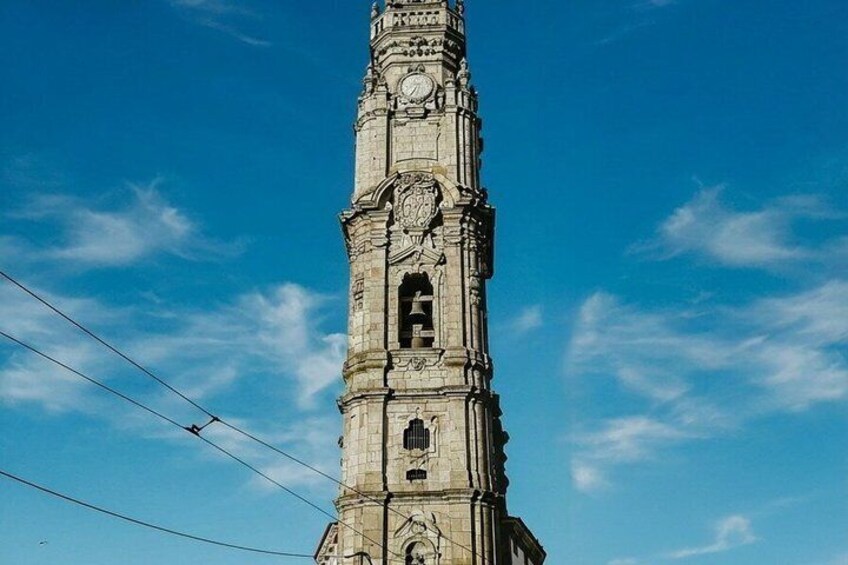 Ett högt, utsmyckat klocktorn med detaljerade sniderier och en klarblå himmel i bakgrunden. 5