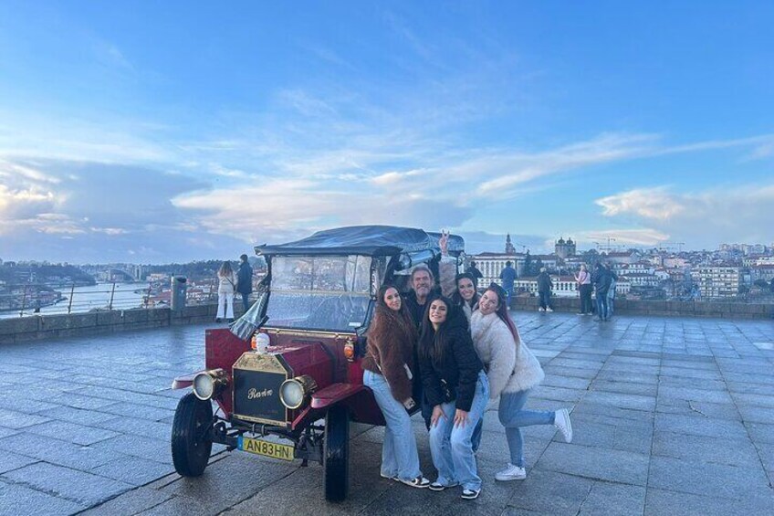 Een groep mensen poseren met een oldtimer op een promenade aan het water. 4