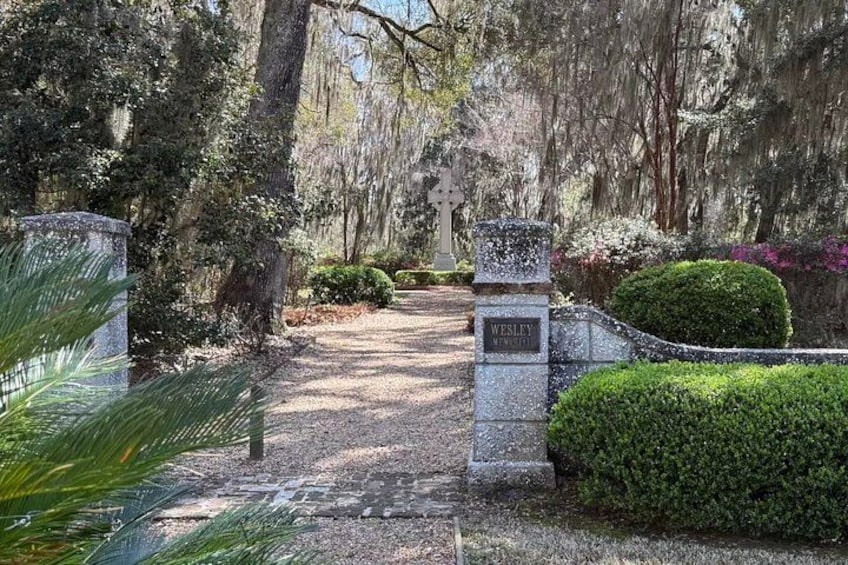A cemetery entrance with a cross, a stone marker, and well-maintained greenery. 2
