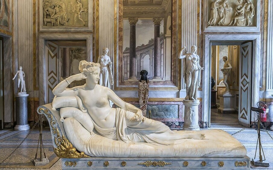 A classical sculpture of a reclining woman on a chaise longue, surrounded by classical statues and architectural details. 5