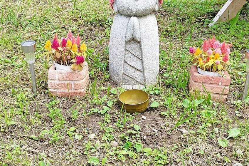 A stone statue with a bow, surrounded by brick planters with colorful flowers, and a brass bowl in the center. 4