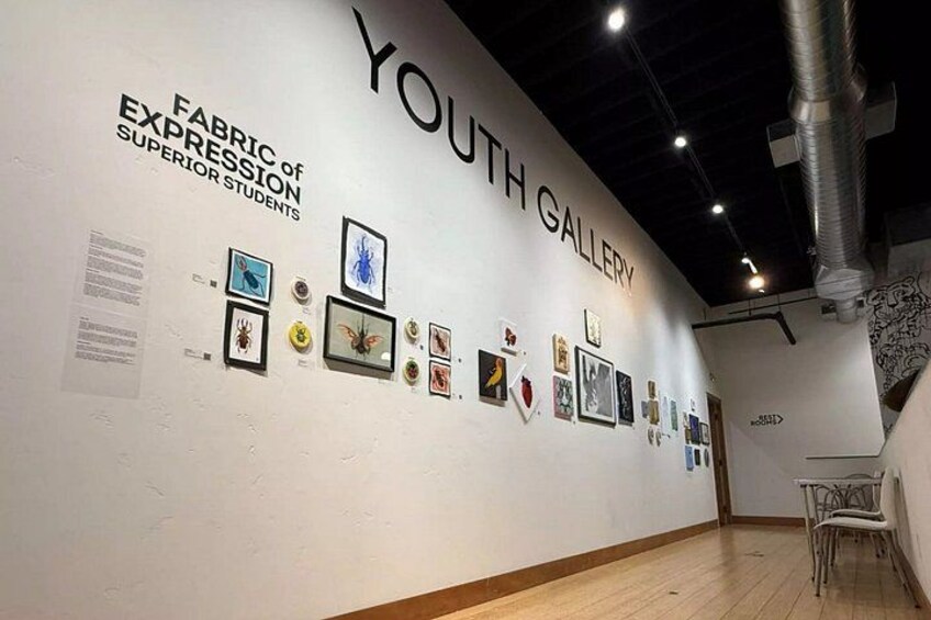 An art gallery with a white wall displaying various framed artworks. 2