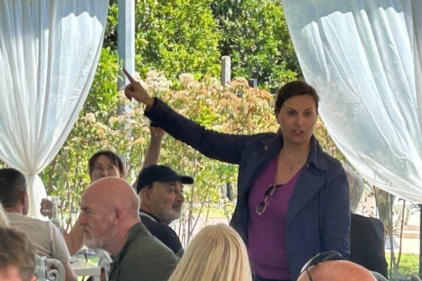 A person gesturing in an outdoor setting with white drapes and trees in the background. 3