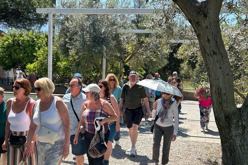 A group of people walking along a pathway in a park with trees and a white pergola structure. 5