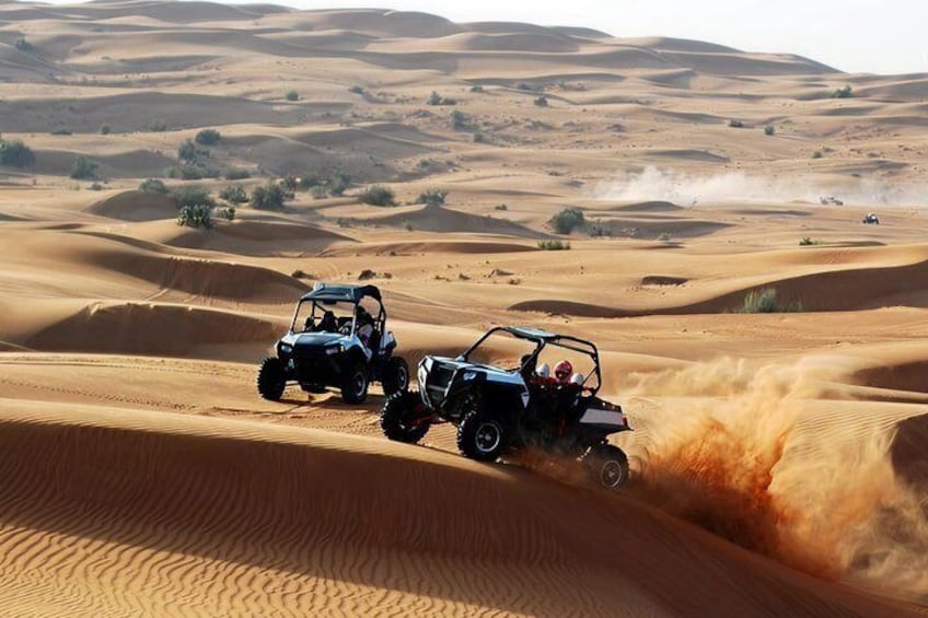 Two off-road vehicles navigating sand dunes in a desert landscape. 2