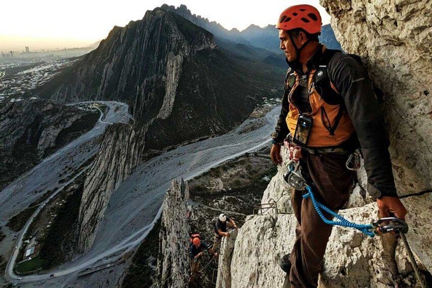 A person climbing a mountain with a rope, a rocky path, and a valley in the background. 1