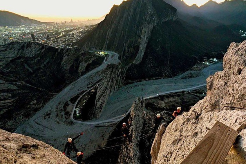 A mountainous landscape with a winding road, rocky terrain, and a group of people climbing a steep rock face. 3
