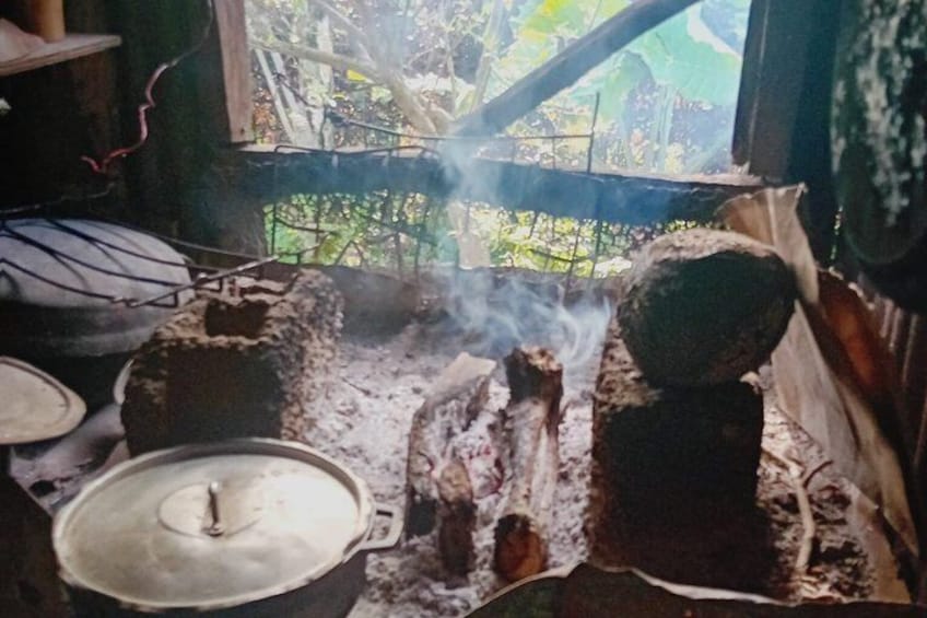 Une cuisine traditionnelle avec un pot sur un réchaud, un four en briques et de la fumée s'élevant du feu. 5