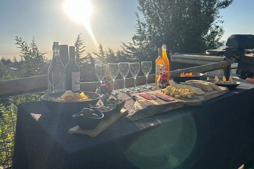 An outdoor dining setup with a table, wine bottles, glasses, and food. 3