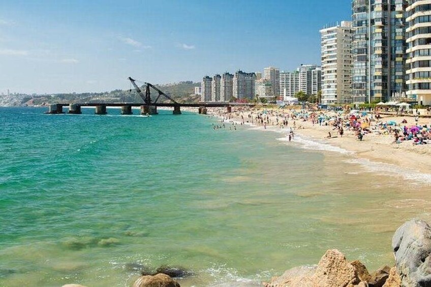 A beach with clear turquoise water, a bridge, and high-rise buildings in the background. 5