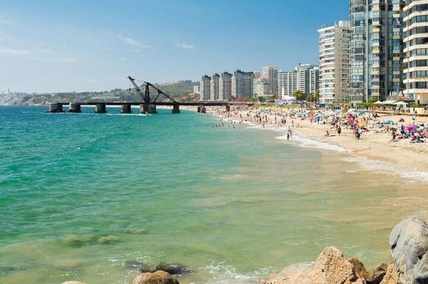 Una playa con agua cristalina, un puente y edificios altos al fondo. 5