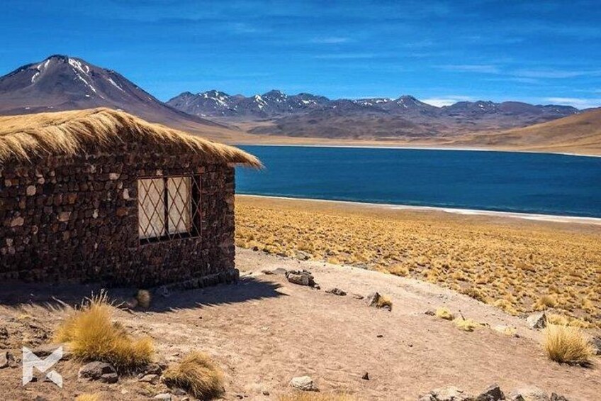 Une cabane à toit de chaume au bord d’un lac, avec des montagnes en arrière-plan. 4